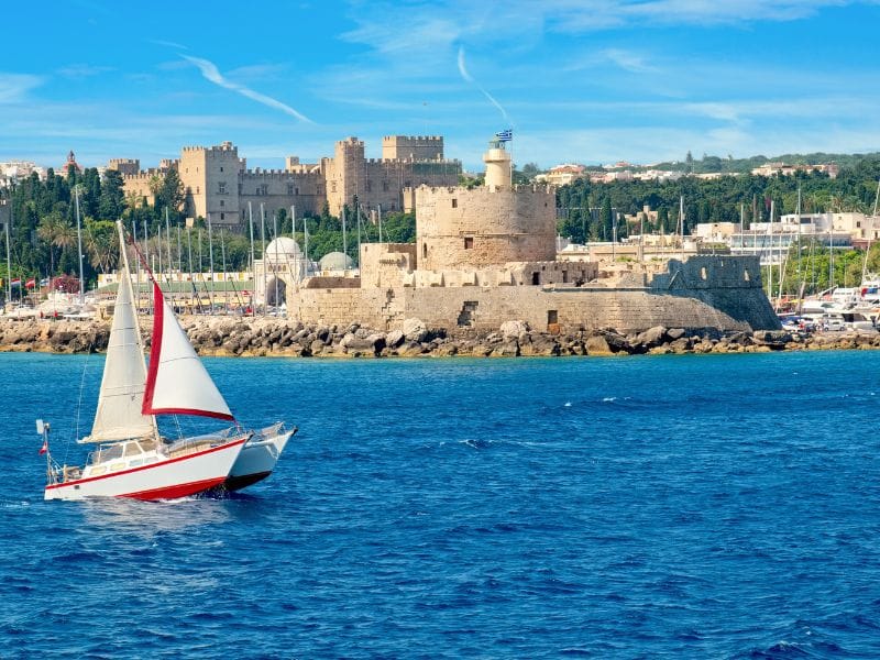 Sailboat near the medieval harbor and fortress during Rhodes Boat Trips.