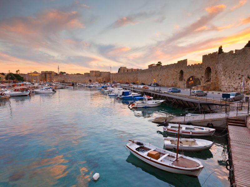Sunset harbor and medieval walls featured during Rhodes Boat Trips.