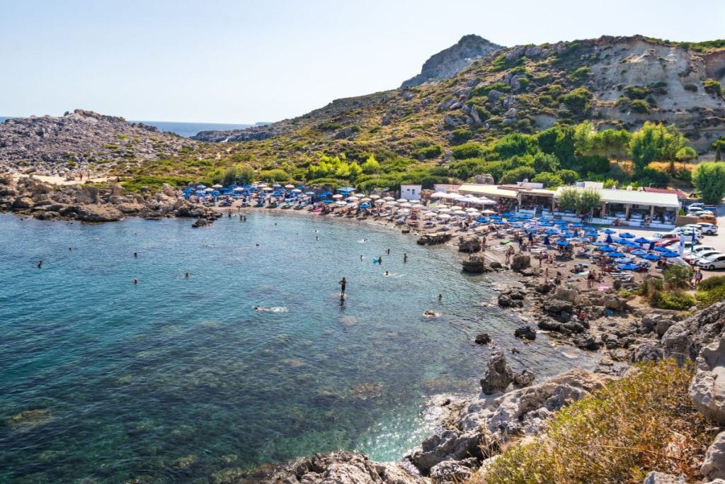 Scenic bay with turquoise waters, rocky coastline, and beachside activity, showcasing one of the most popular coastal settings among the best experiences in Rhodes.