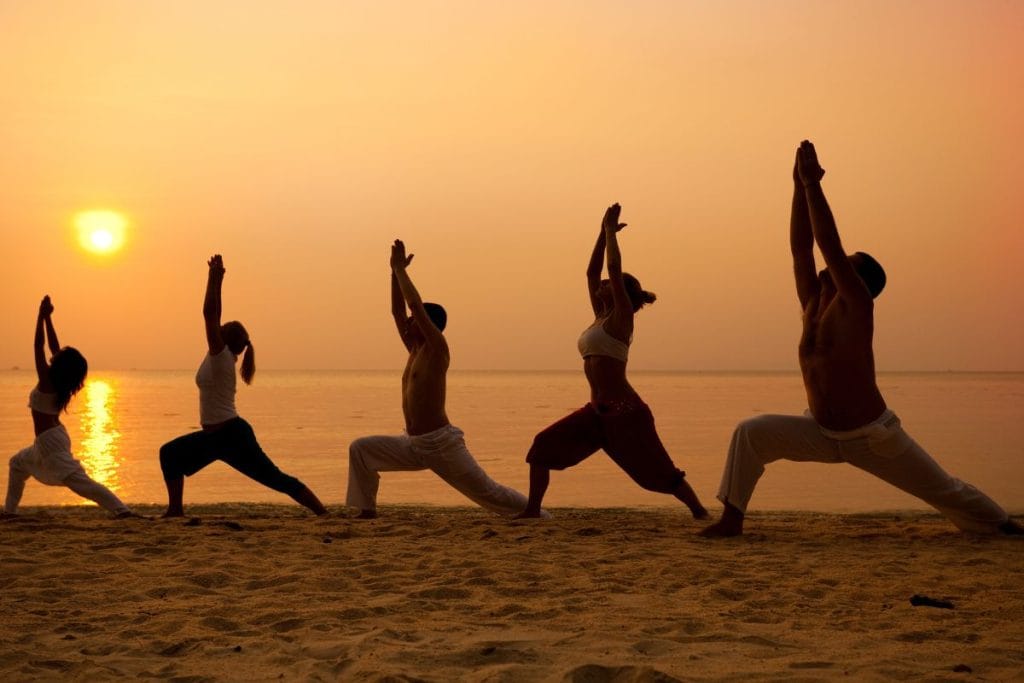 Group practicing yoga on a beach at sunset during unique experiences in Rhodes.